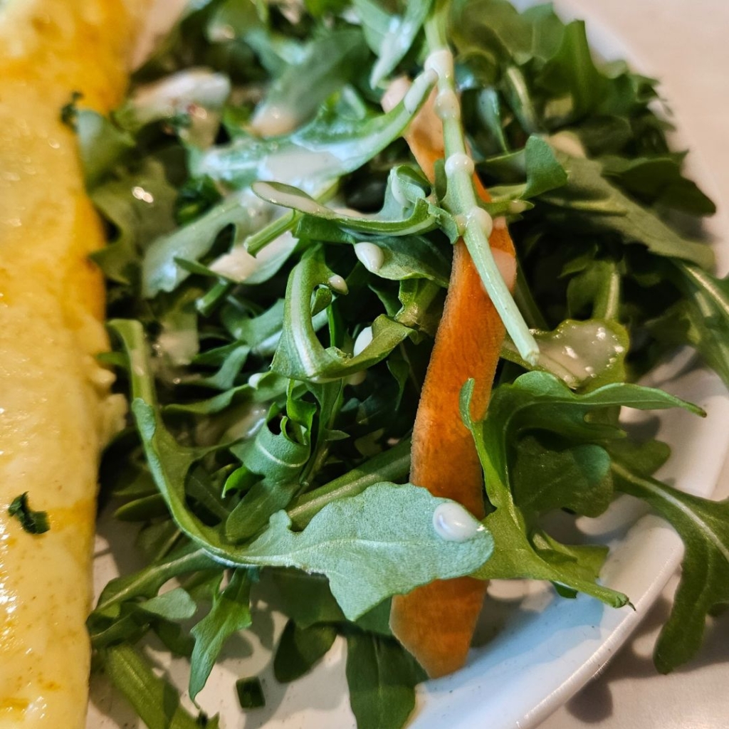 close up picture of arugula crisp salad with light drizzle of salad dressing