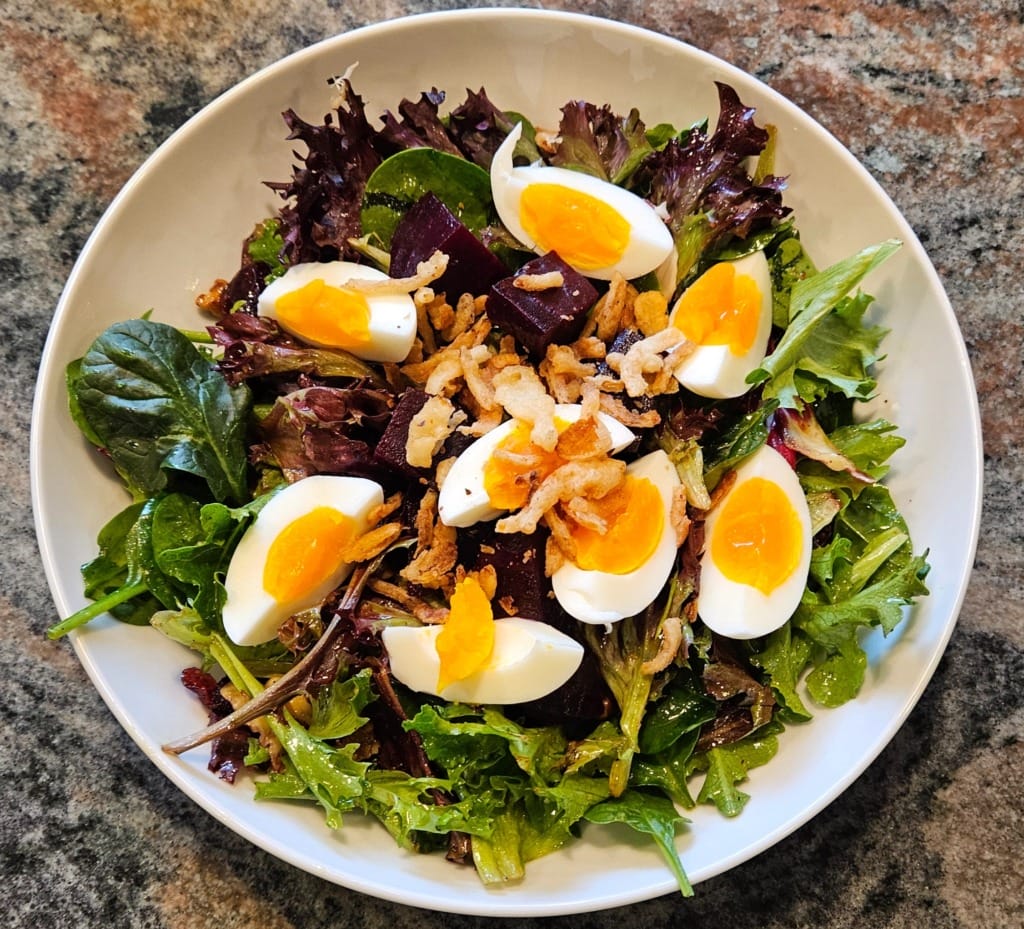 Fresh salad topped with slices of boiled egg on a white plate.