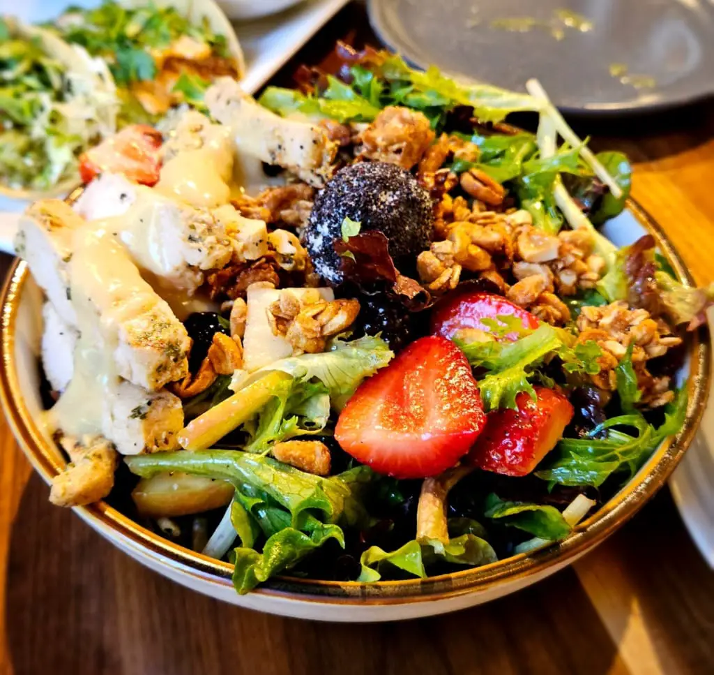 Colorful mixed salad topped with chicken, strawberries, and walnuts, drizzled with creamy dressing, and served in a ceramic bowl.