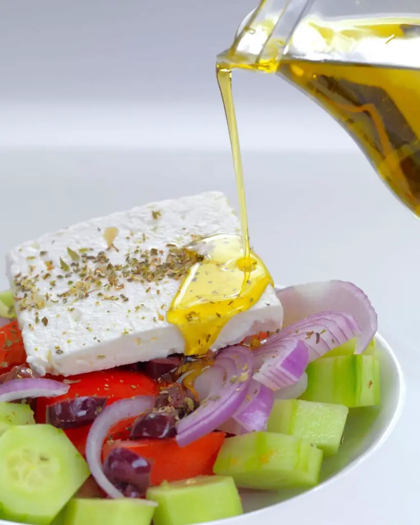 Greek salad being poured with olive oil from a bottle.