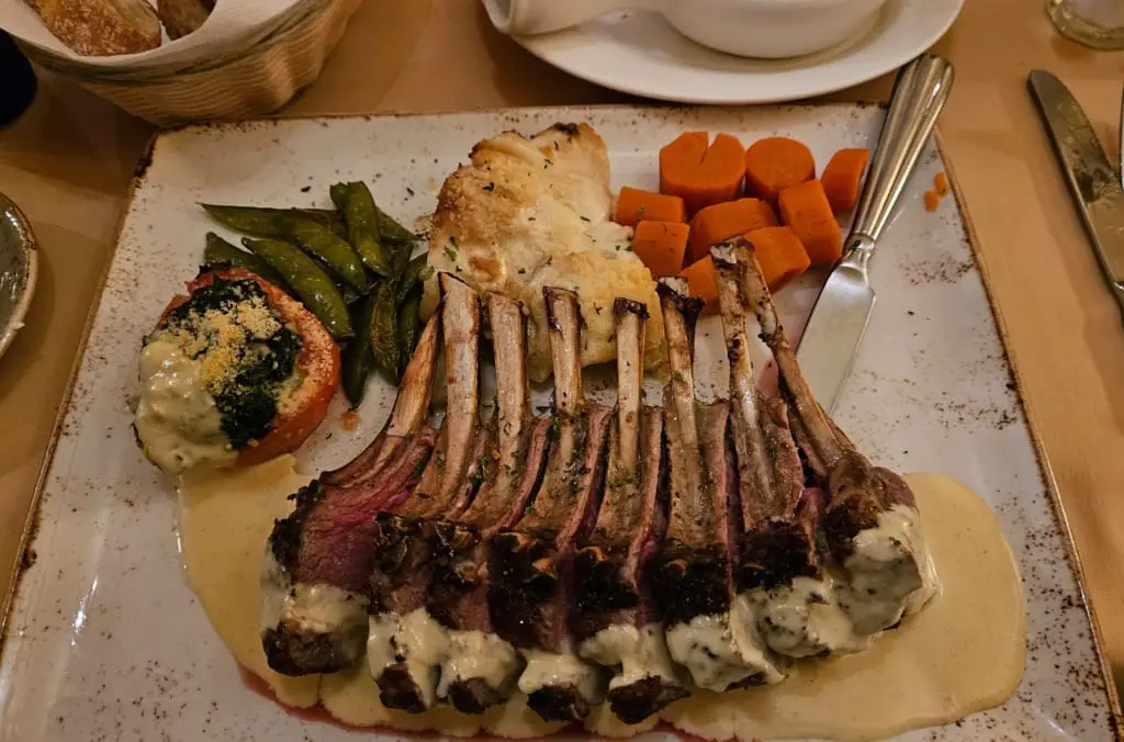 Lamb chops on a plate with chopped carrots green beans and mashed potatoes.