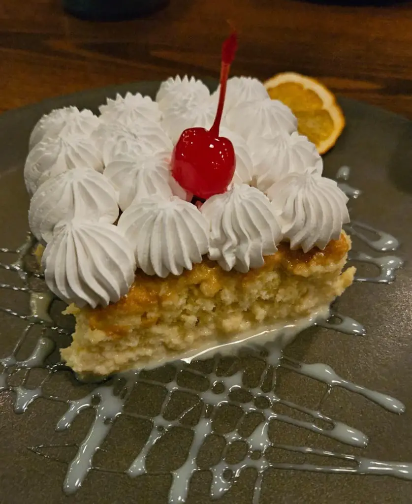 Slice of cake topped with Chantilly cream and cherry on a plate.