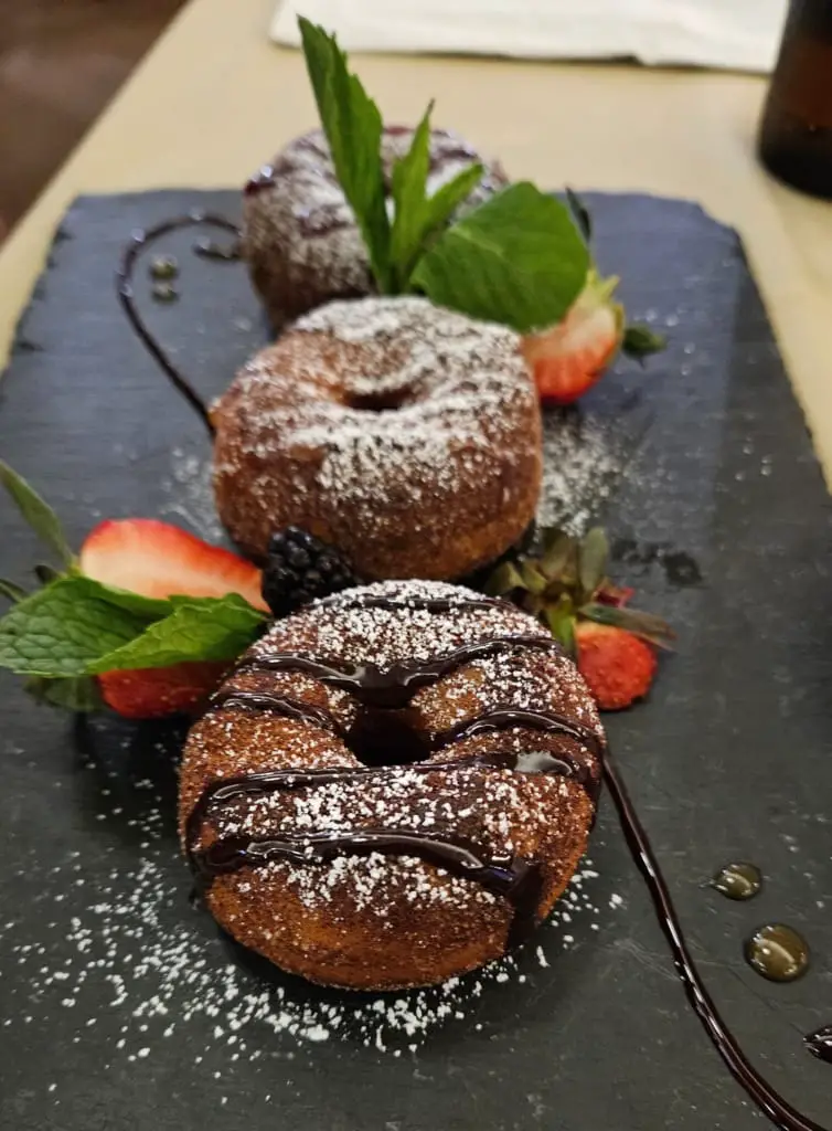 Chocolate donuts on a serving board sprinkled with powdered sugar on top.